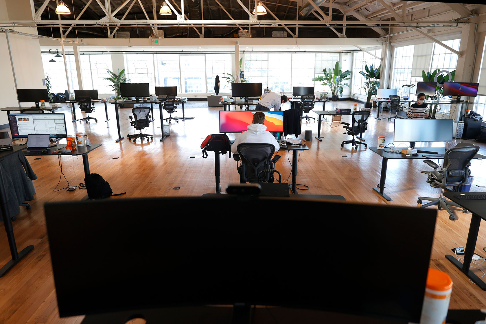 Photo shows a view of an open office with mostly empty desk setups, and a large window in the back of the room