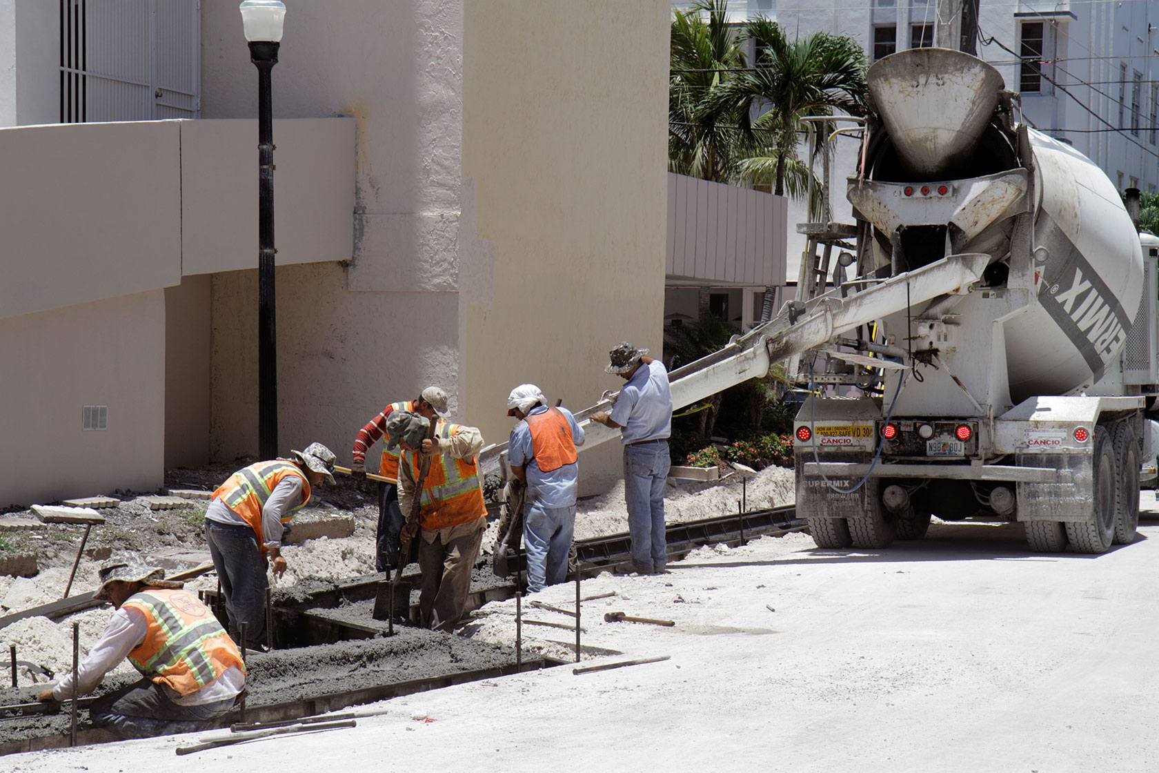 Construction workers use a cement mixer to pour concrete onto a road.