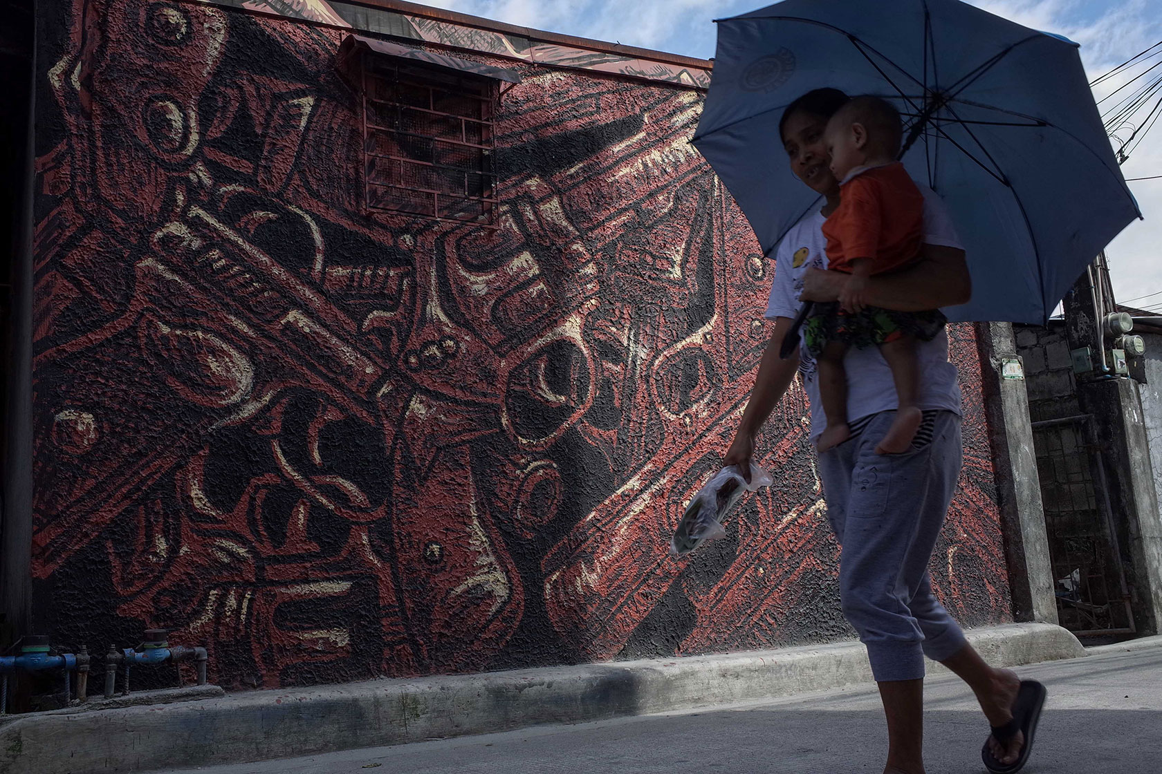 A woman carrying her child walks past a mural depicting guns.