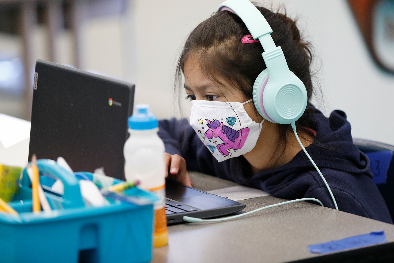 Student wearing face mask and headphones works on computer