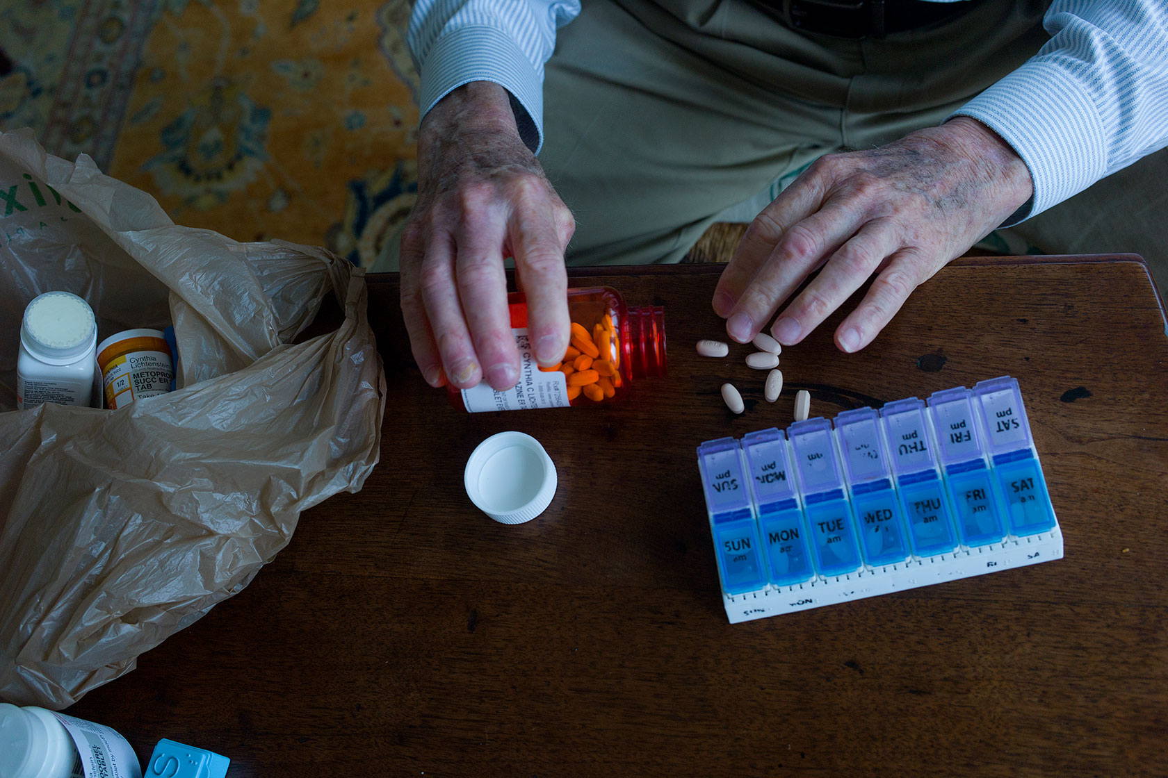 Close-up on hands tipping pills out of a bottle onto a table; pill organizer nearby