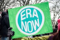 Photo shows a closeup of a green sign with the phrase "ERA NOW" printed on it