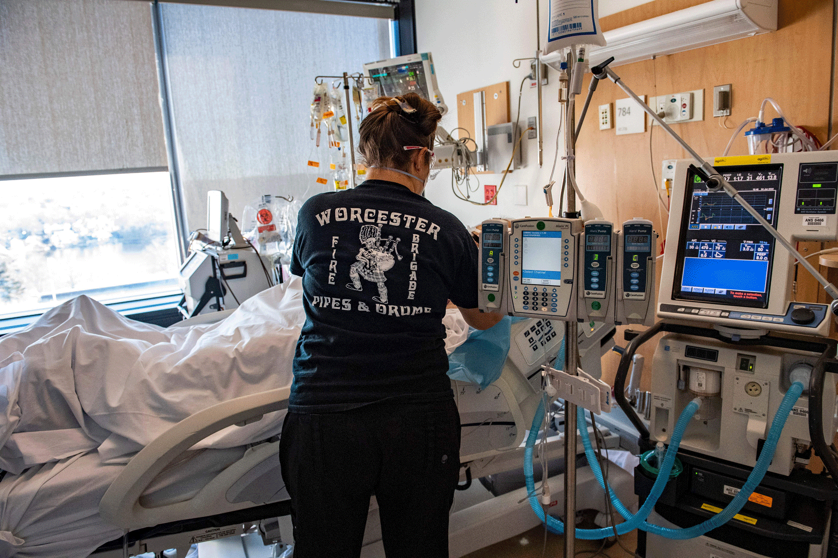 The back of a nurse is seen as they tend to a patient in a hospital bed.