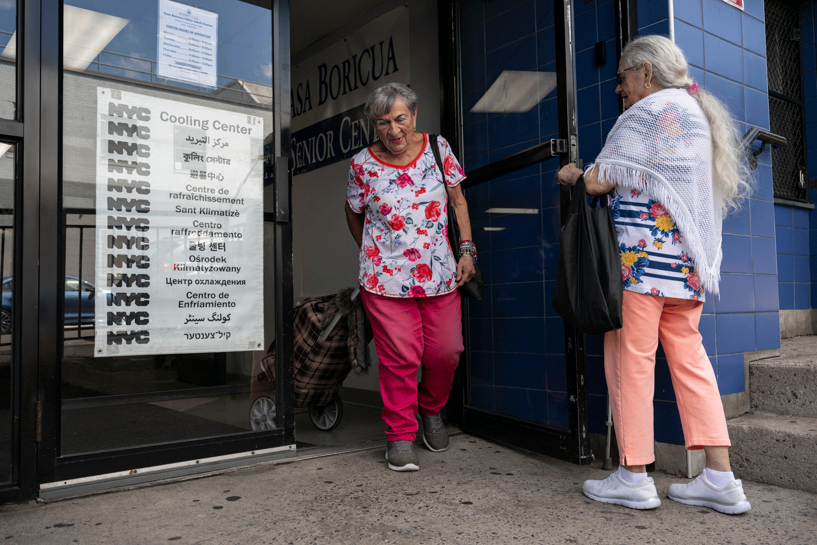 One older adult is seen holding the door open for another as they exit a cooling center.