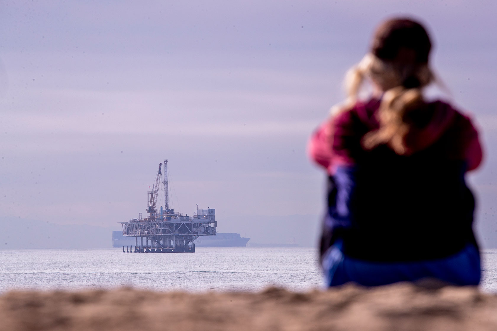 A person looks toward container ships and oil platform Esther.