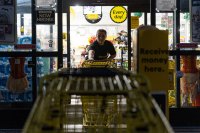 An employee pushes shopping carts out the front doors of a dollar store.