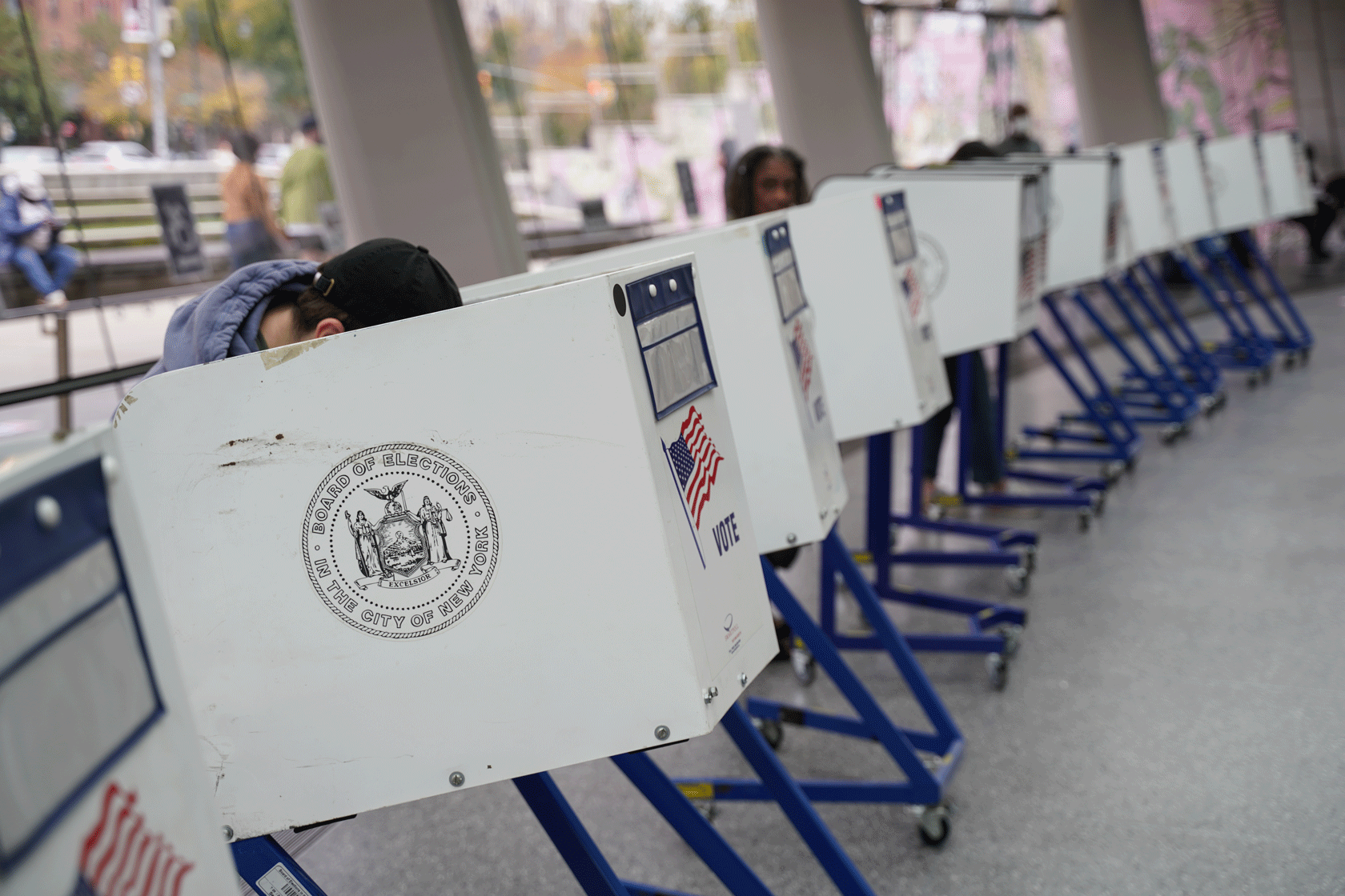 A row of polling booths is seen with some voters crouched behind them.