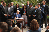 President Biden is seen at a desk signing proclamations, surrounded by others.
