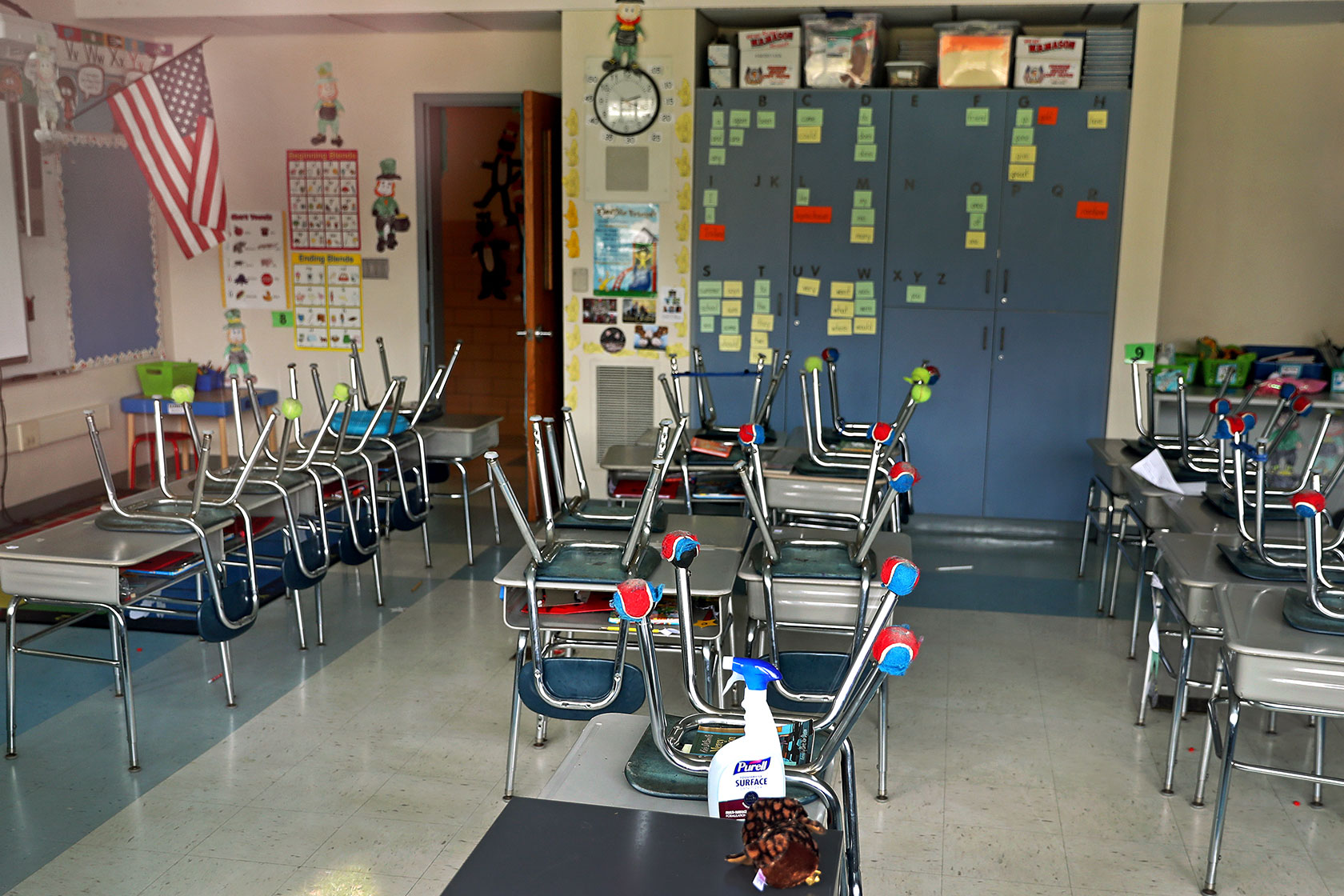 Photo shows multiple school chairs sitting upside down on top of desks