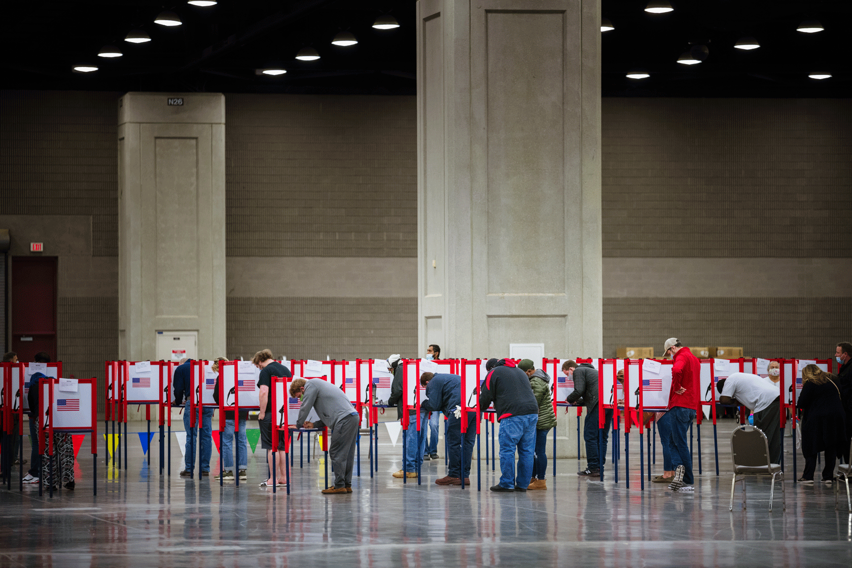 A relatively large number of voters are seen standing behind voting booths in a big room.