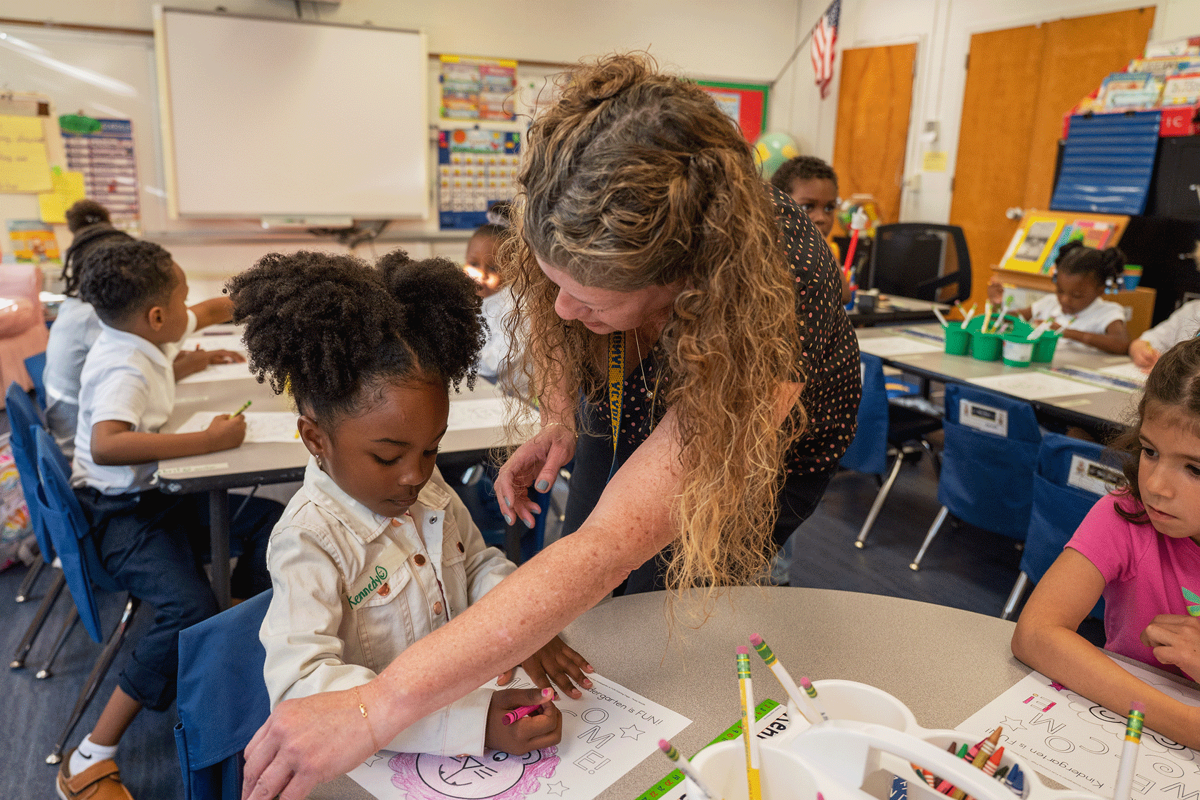 In a classroom full of students, a teacher is seen assisting one of them.