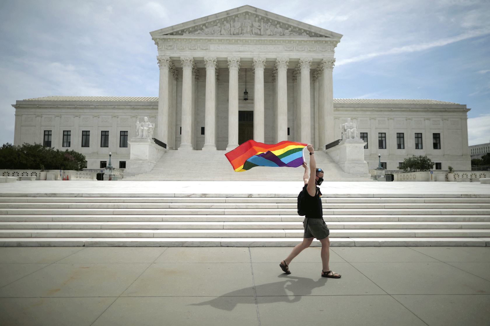 A person carrying a pride flag is seen walking in front of the U.S. Supreme Court building.