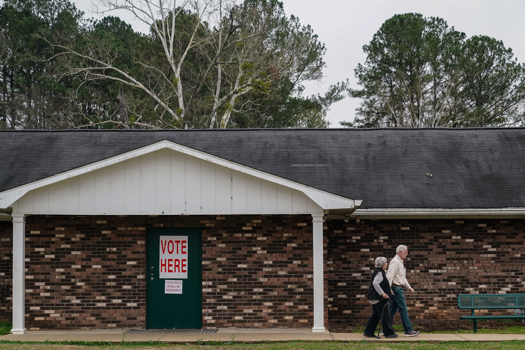Two voters are seen walking out of a brick building that has a green door with a 