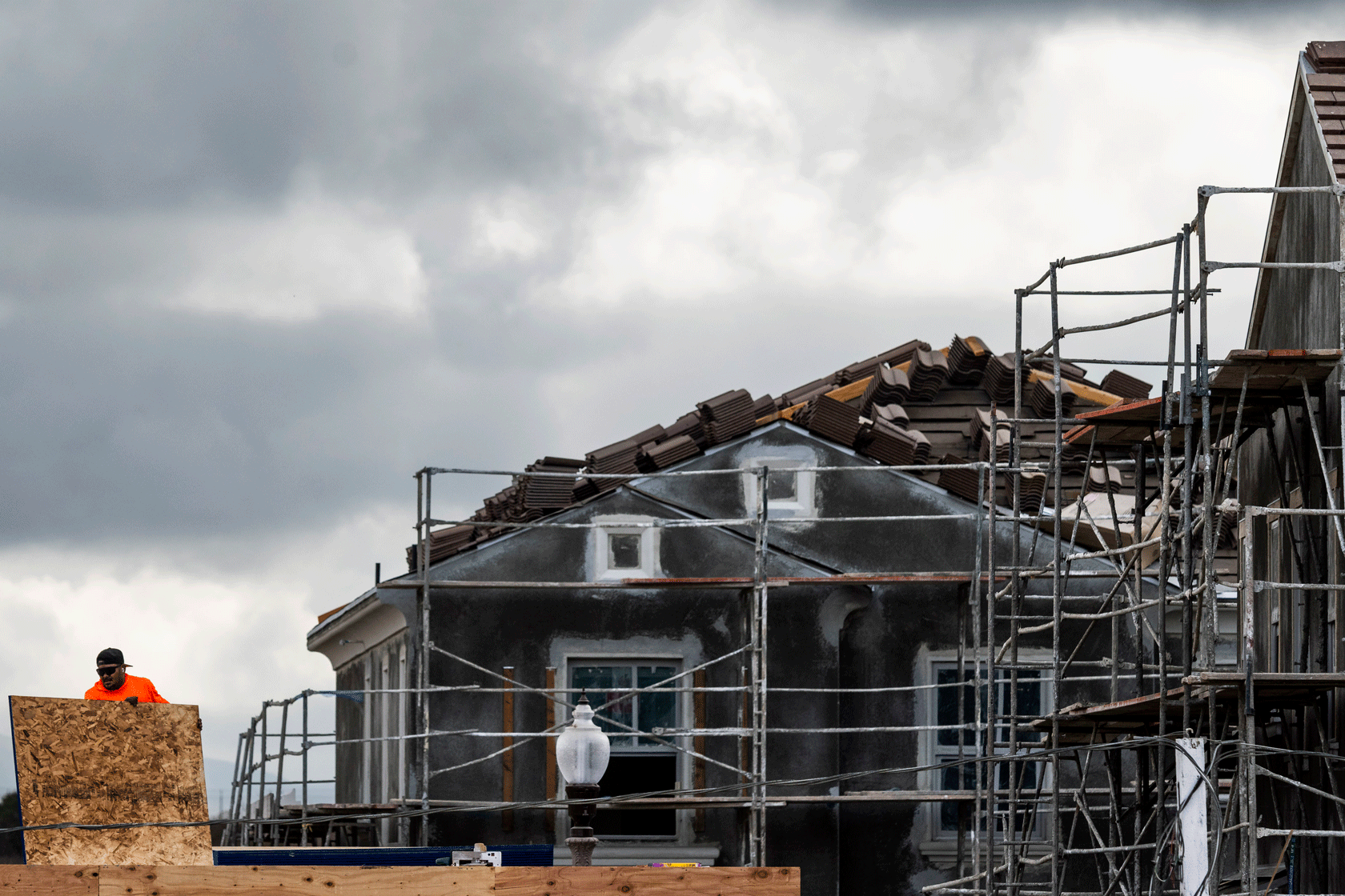 The upper half of a partially constructed house is seen with two workers working on it.