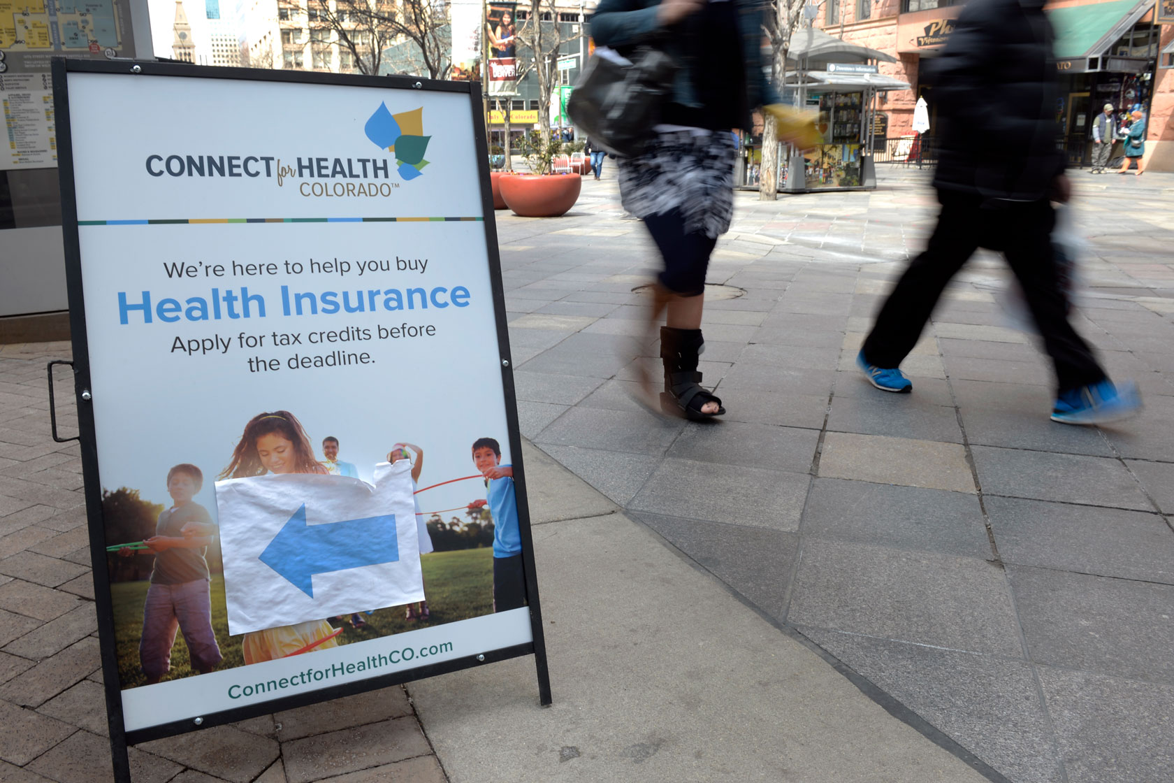Pedestrians walk past a sign encouraging people to sign up for health insurance through the Affordable Care Act.