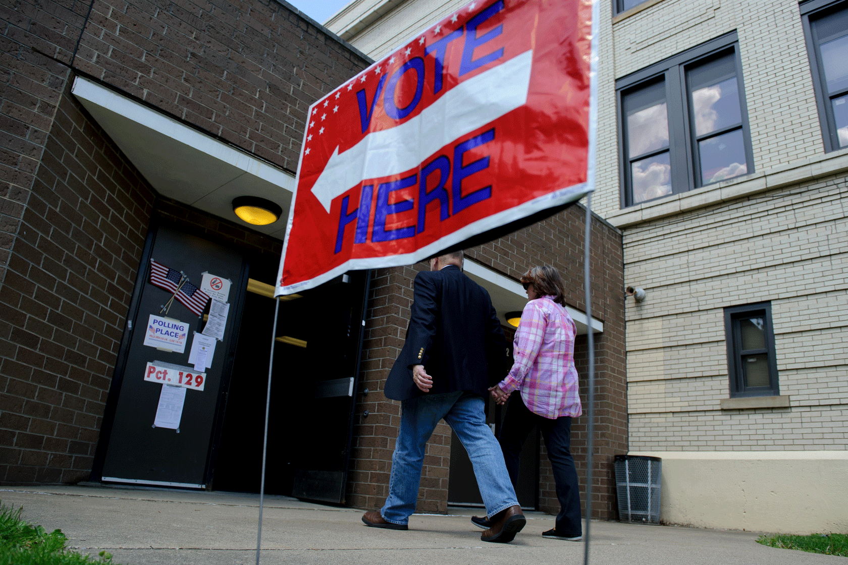 Two people are seen walking into a building behind a sign that reads 