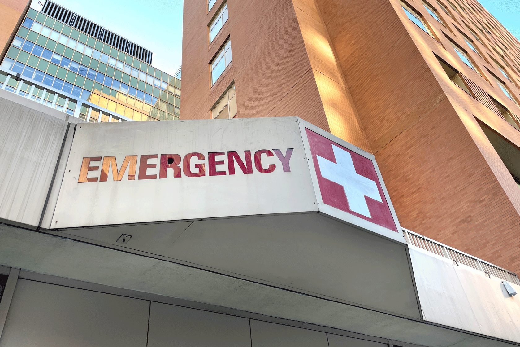 The entrance to an emergency room is seen below a tall hospital building.