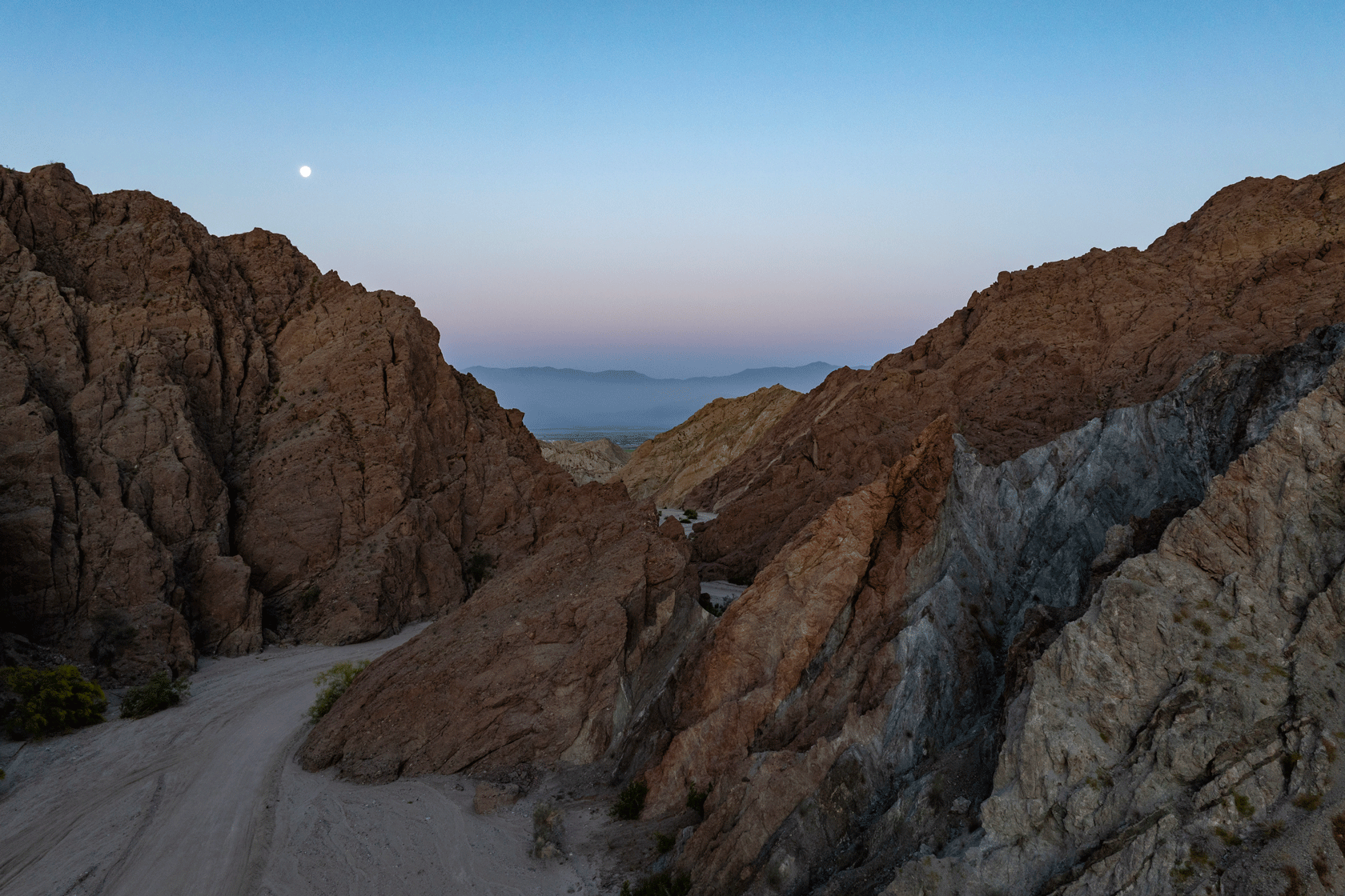 Rocky Mountains are seen in front of a sunset with a sandy path cutting between them.
