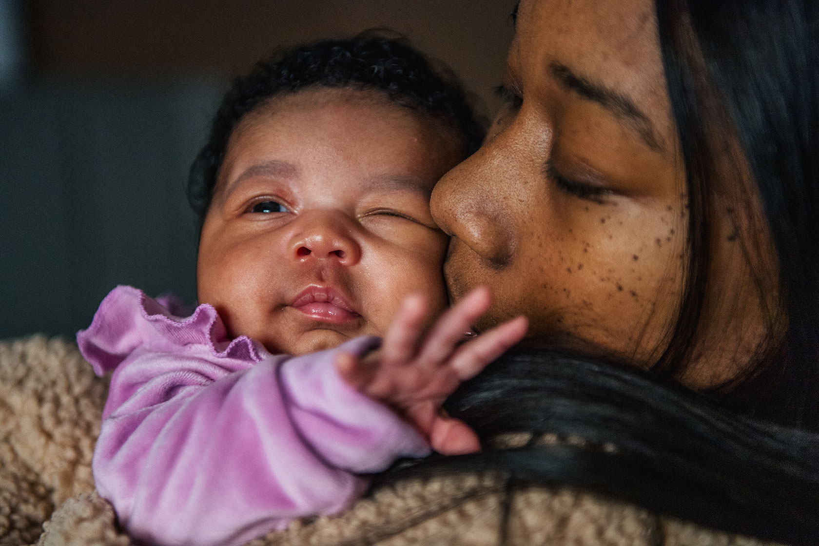 Closeup image showing a mother kissing the cheek of her newborn baby