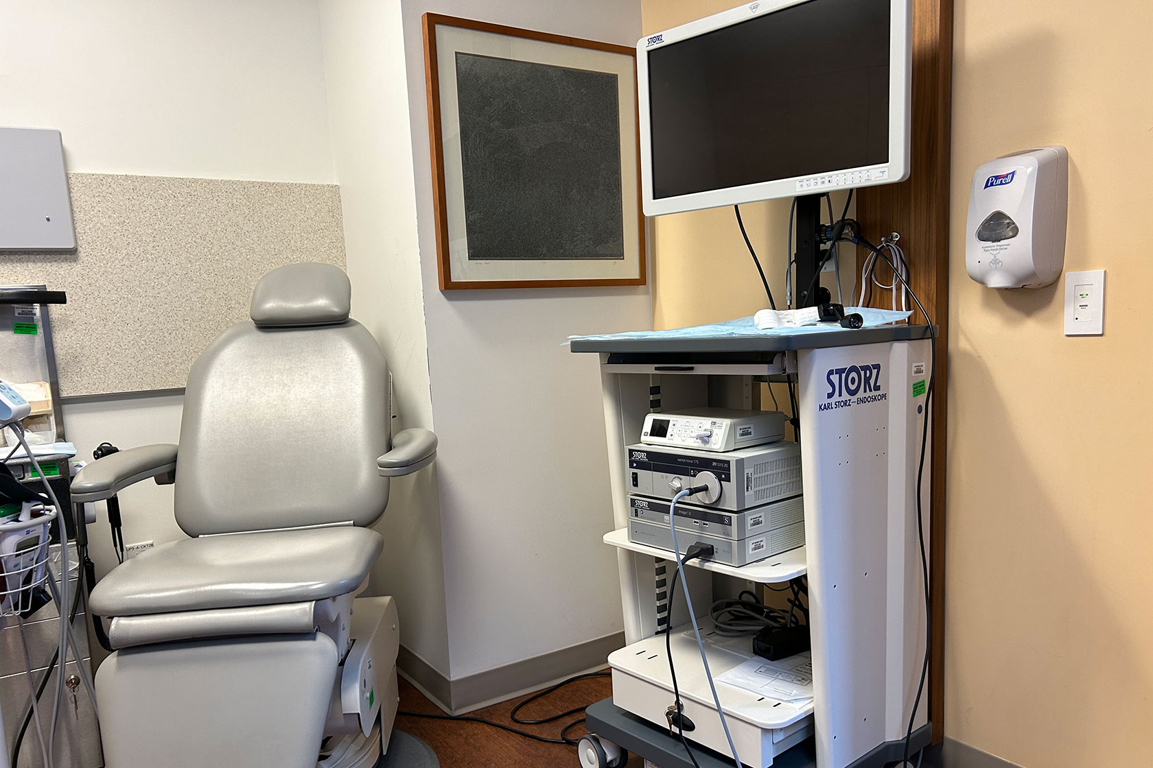 Photo shows an empty medical examination room with a chair and computer screen