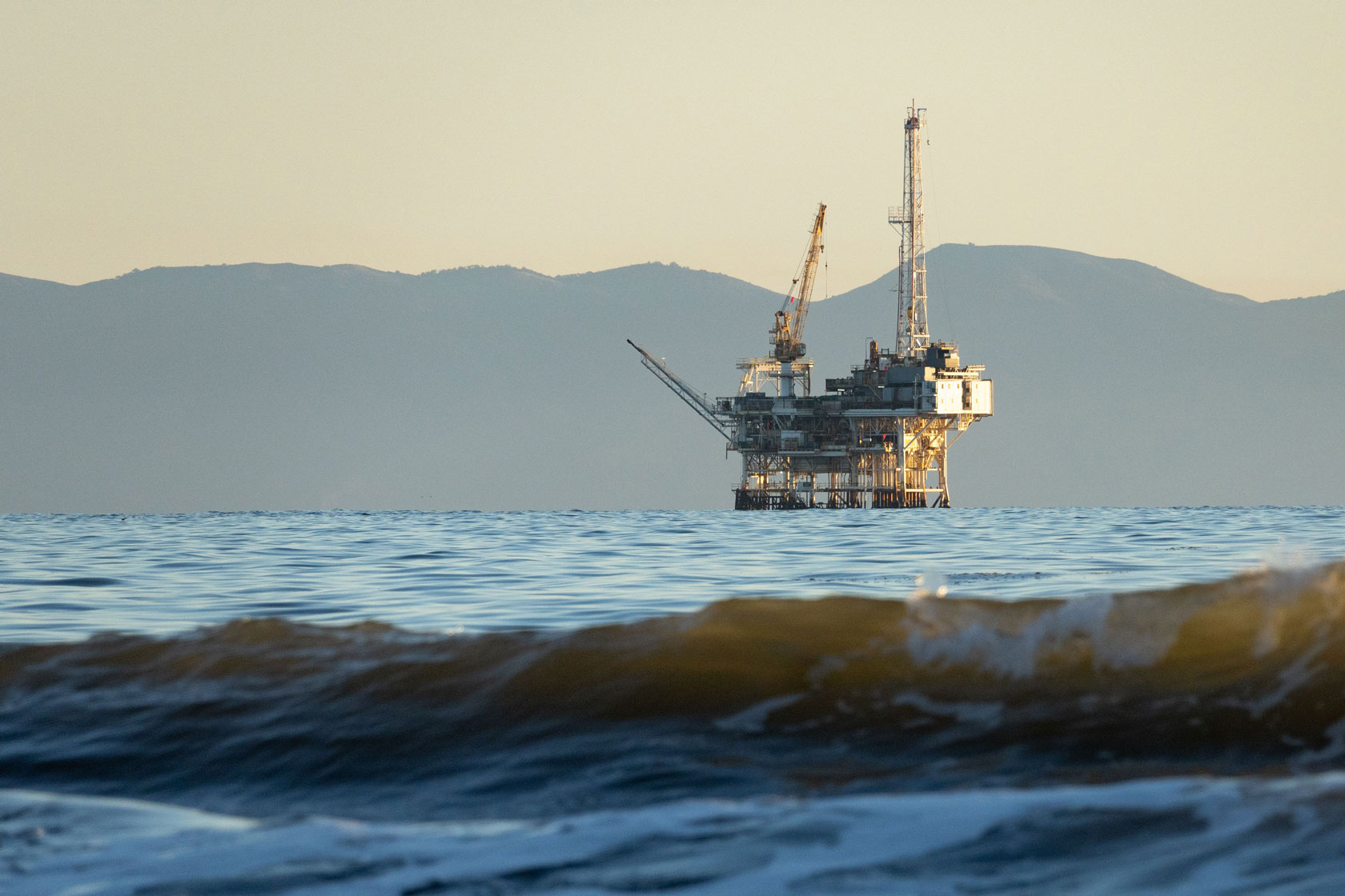 A wave rolls along Santa Barbara Channel in California and an offshore oil platform sits in the distance.