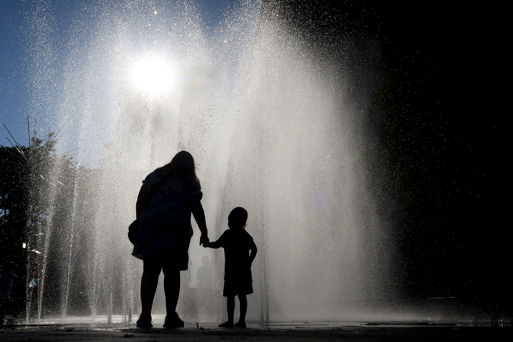 A child and his mother stand in front of a fountain in Hoboken, New Jersey, May 25, 2024.