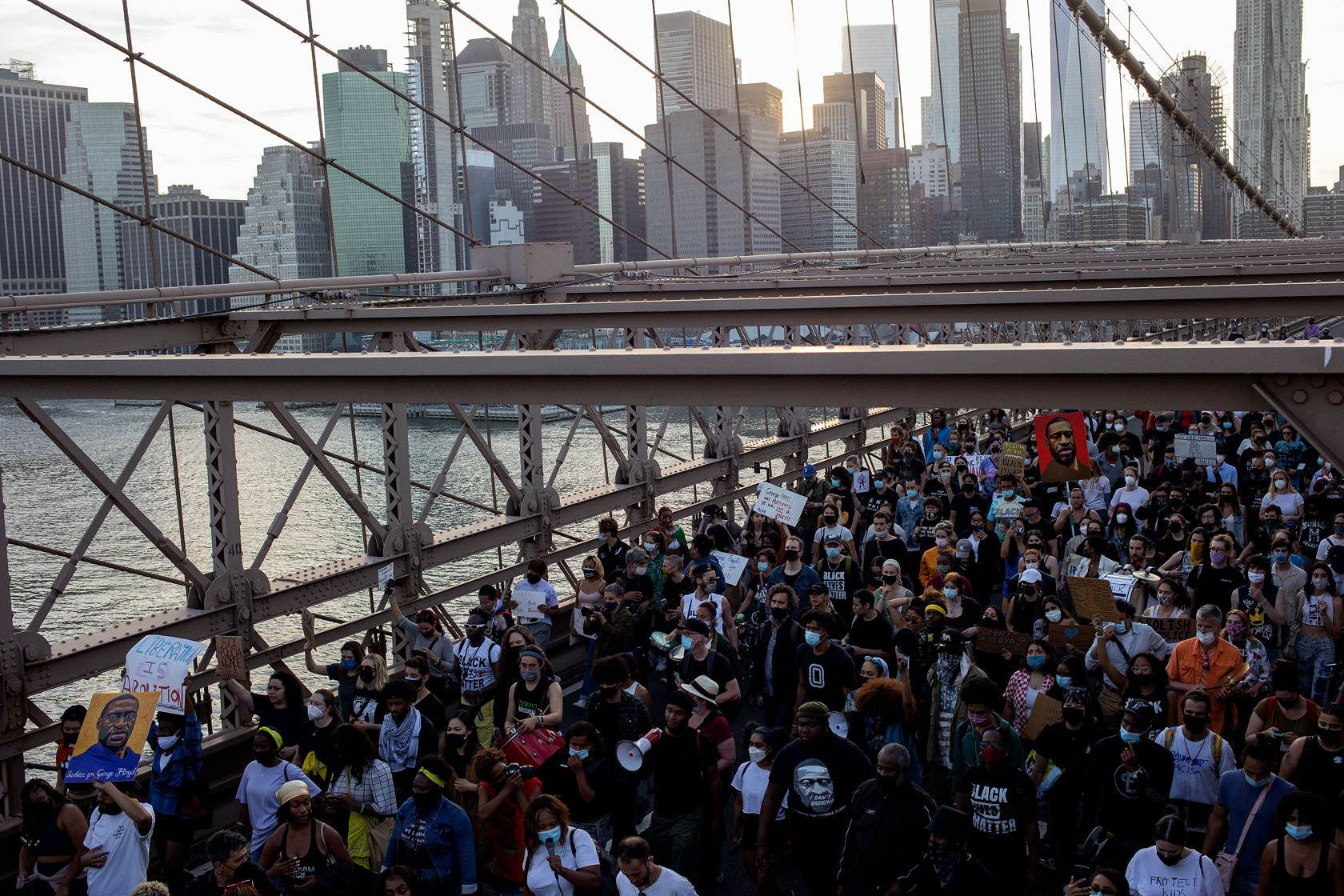 A crowd of demonstrators is seen marching across the Brooklyn Bridge while the sun sets over the Manhattan skyline in the background.