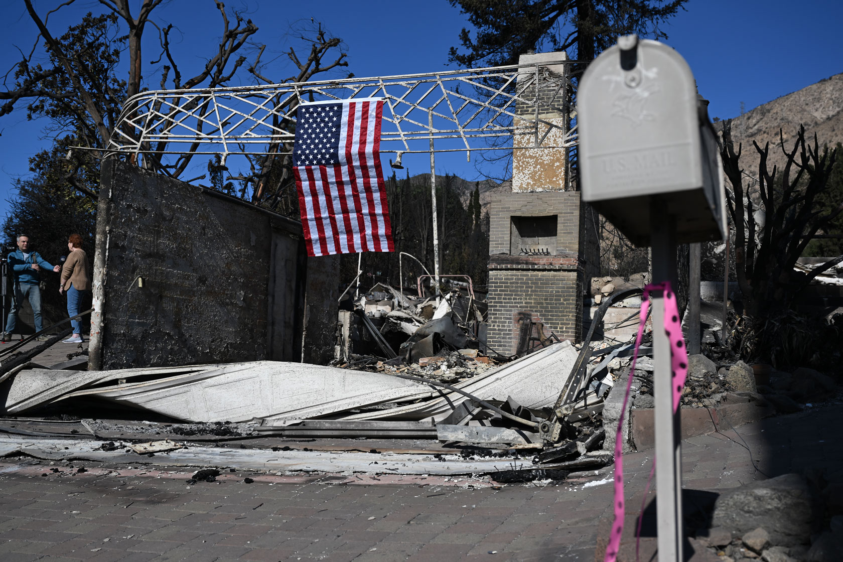A couple stands to the left of the remains of a home burned down in January 2025 during a massive wildfire in and around Los Angeles.
