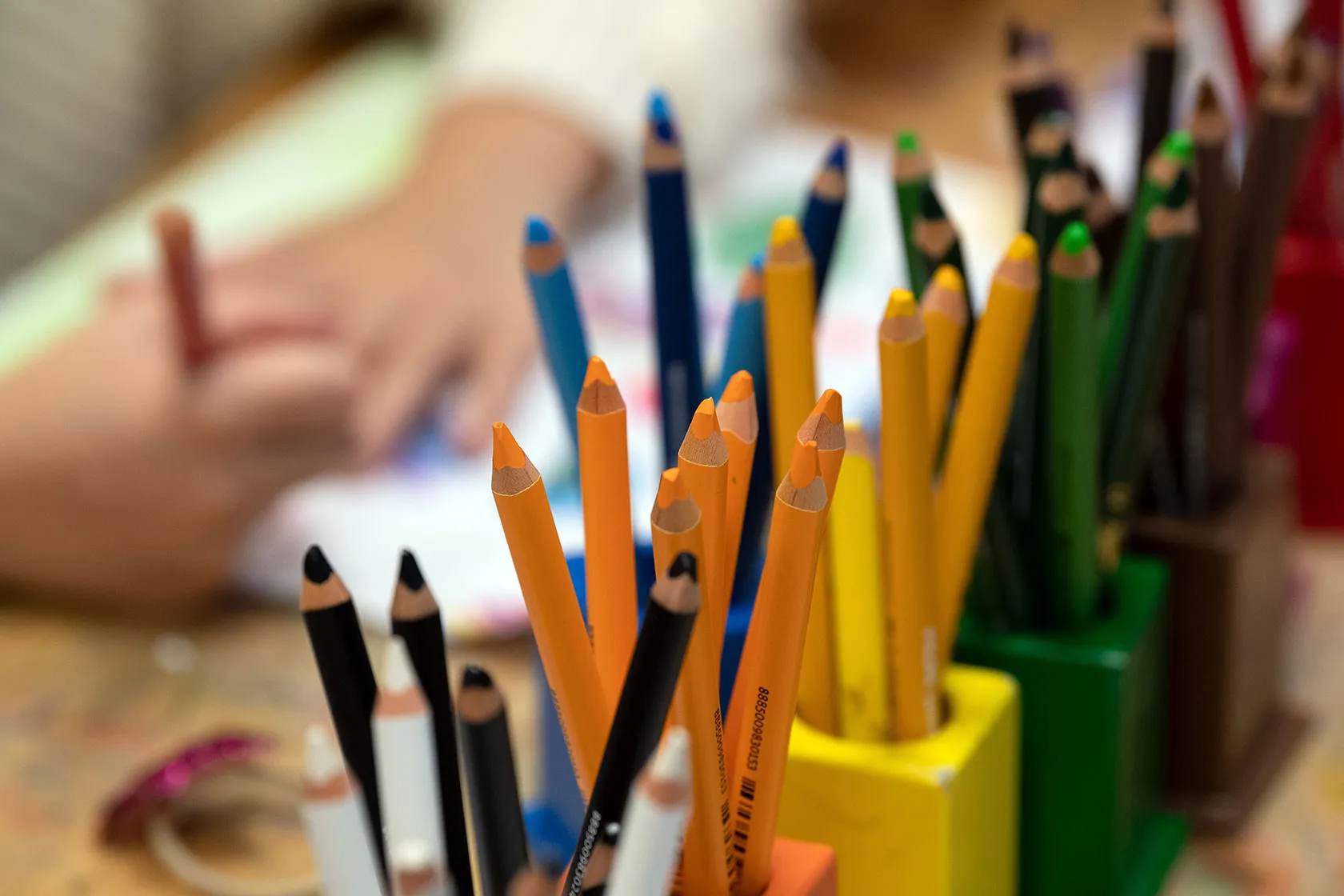 Colored pencils in focus, with a child's hand in the background
