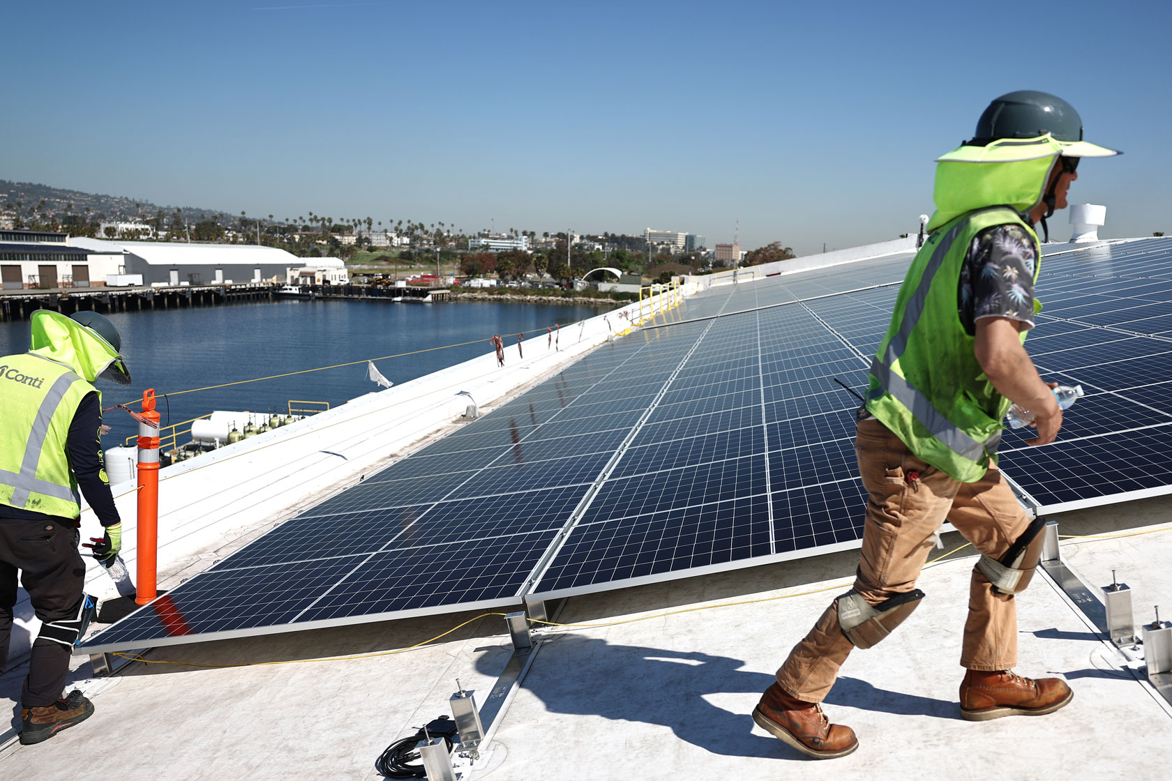 Workers walk along the roof of a building installing solar panels.