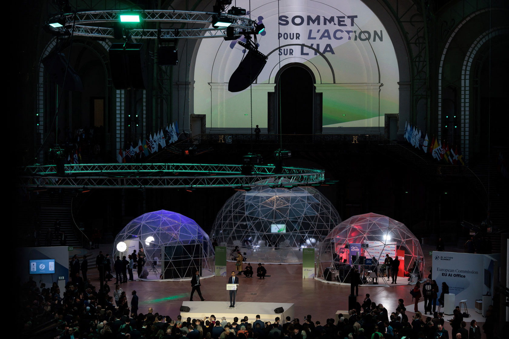 Google CEO Sundar Pichai is seen delivering a speech in a large, dark room.