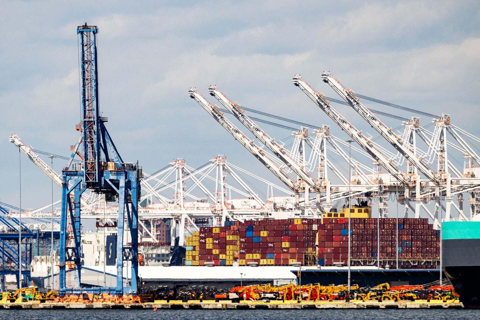 Stacks of shipping containers are seen with cranes in the background.