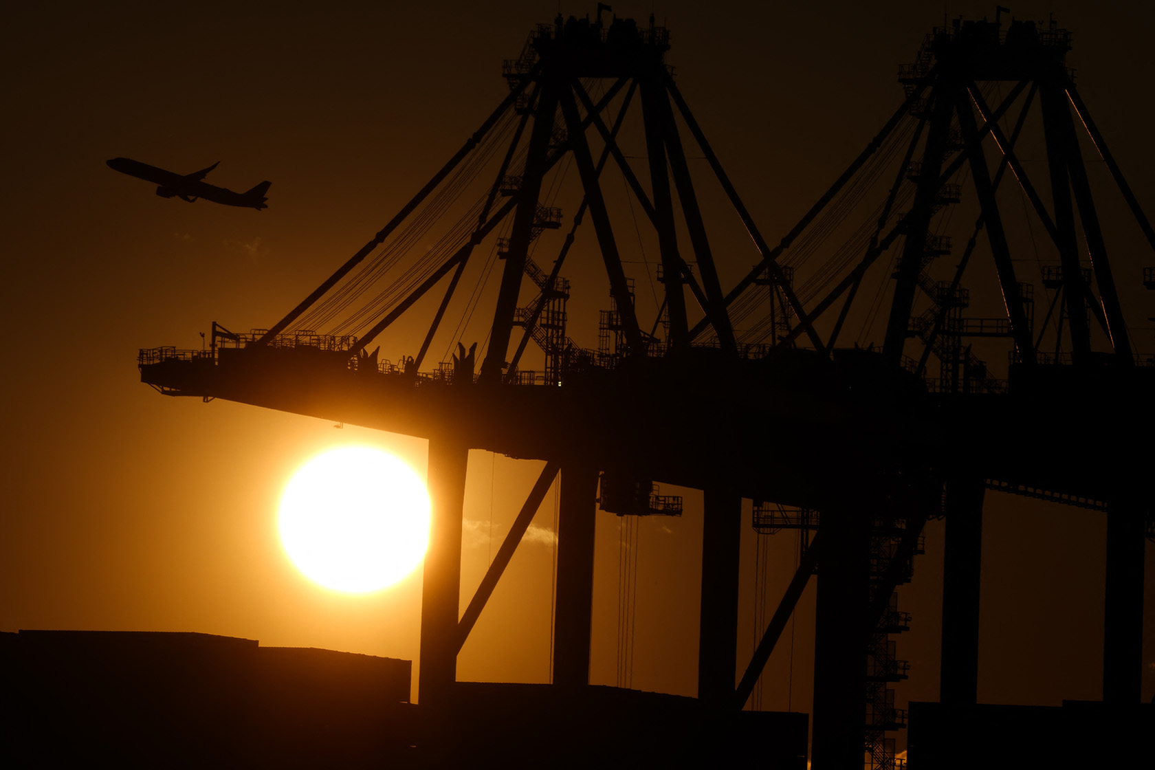 An airplane flies past cranes at the Port Newark Container Terminal.