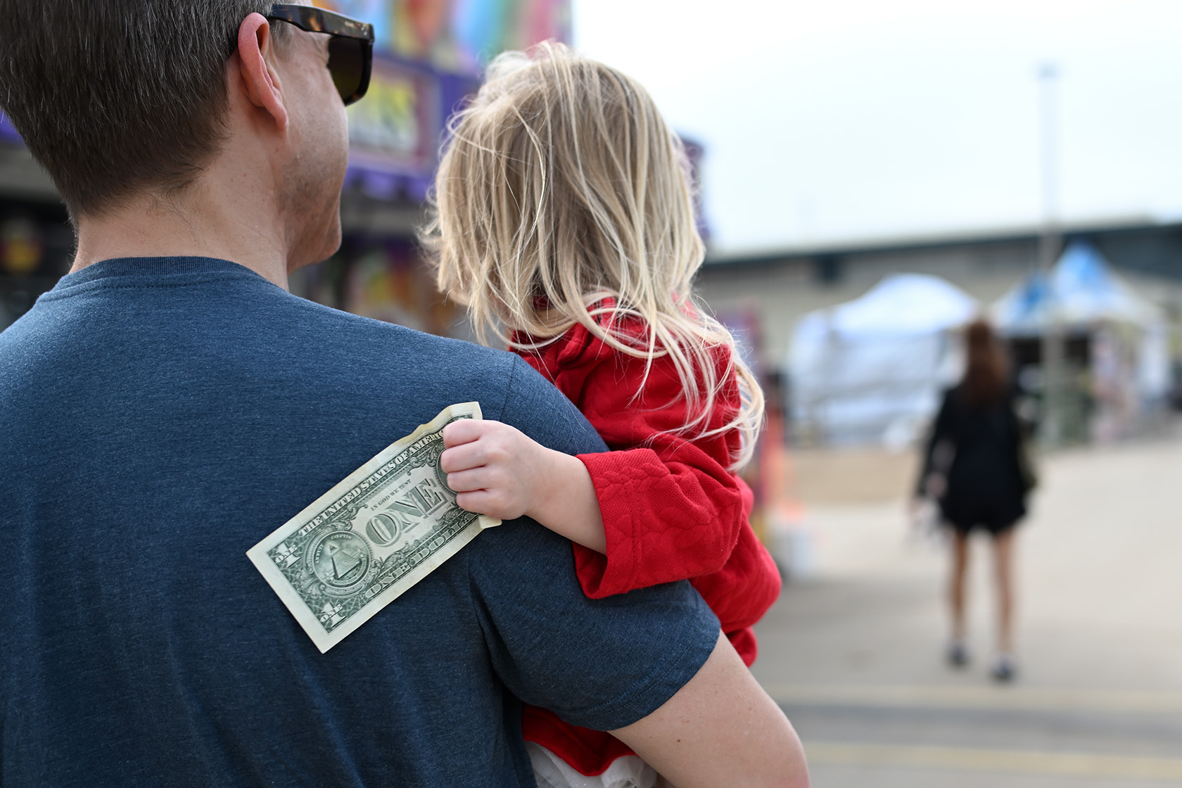A 4-year-old holds a dollar bill while being held by her father.