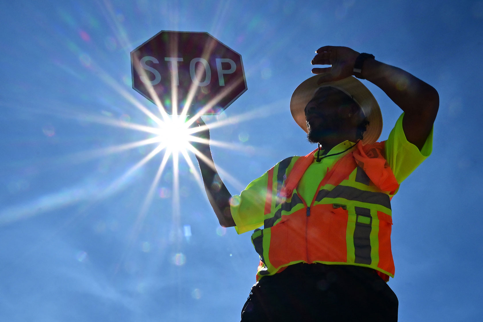 A traffic warden holding up a stop sign with the sun shining behind him