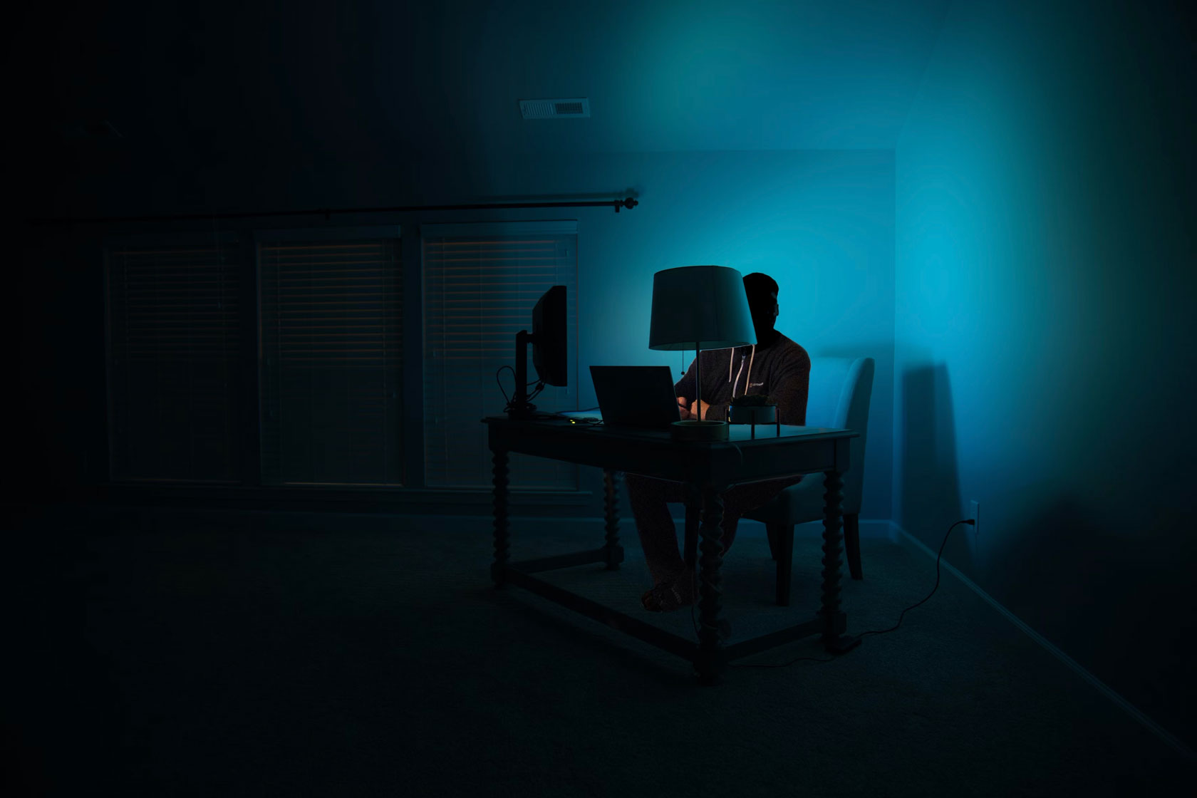 A person sits behind a computer in a dark room.