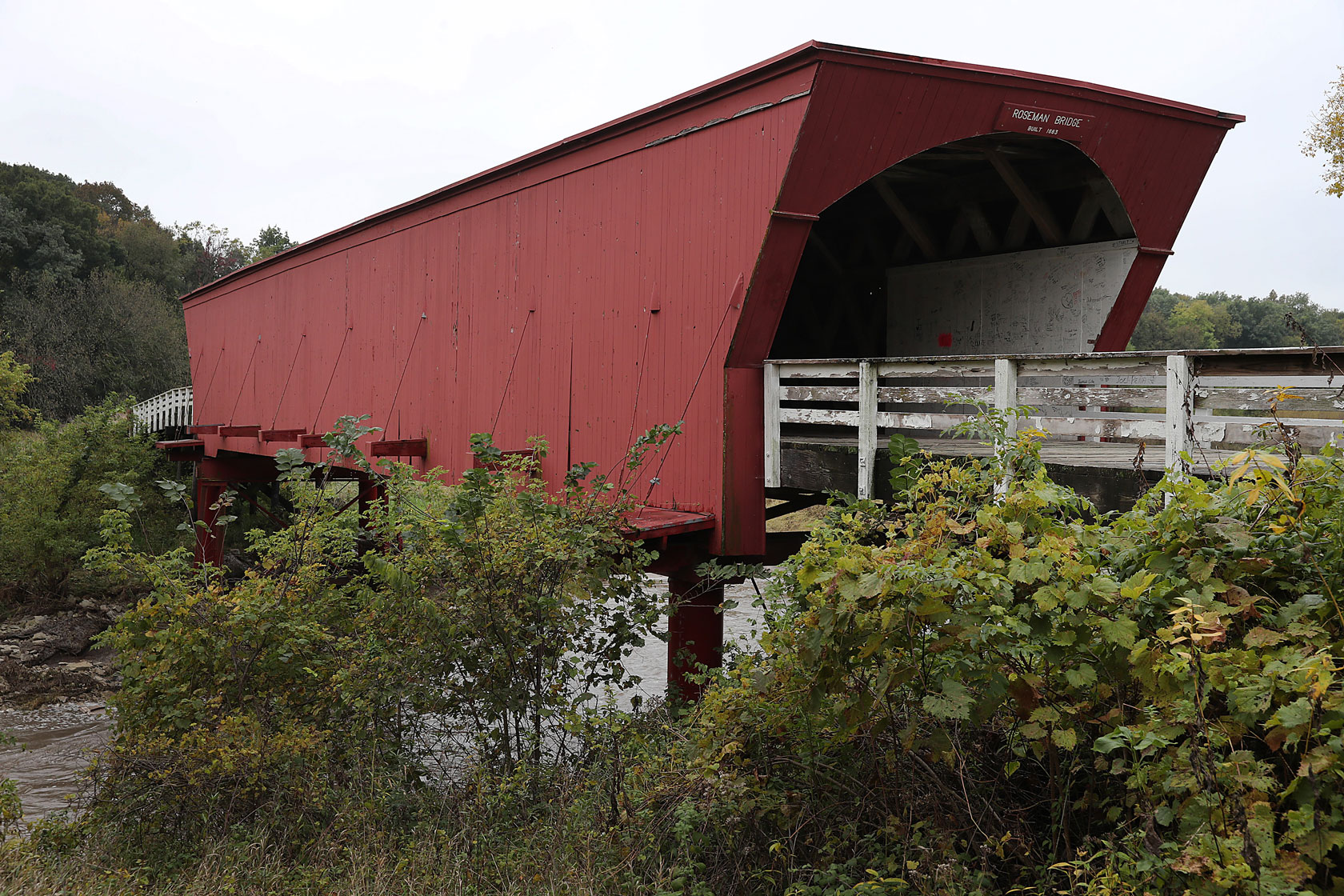 A red covered bridge is flanked by white fencing.