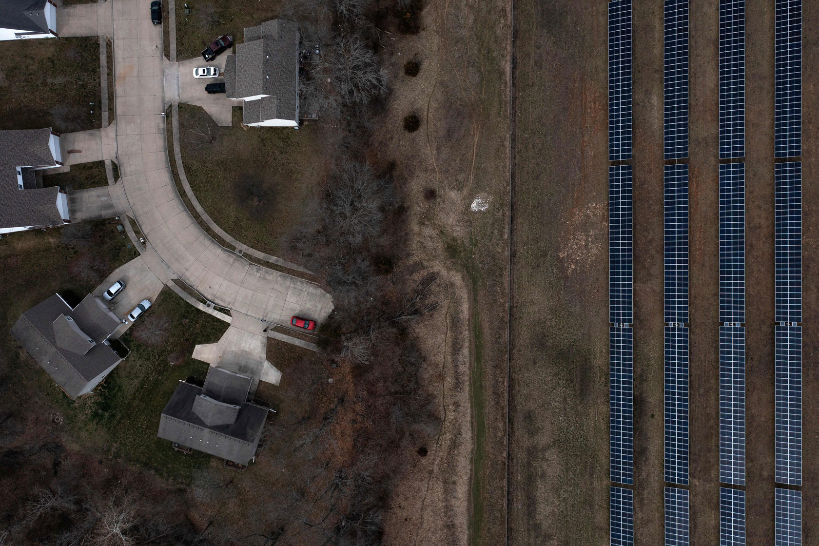 Four long rows of solar panels sit across from a curved street lined with houses.