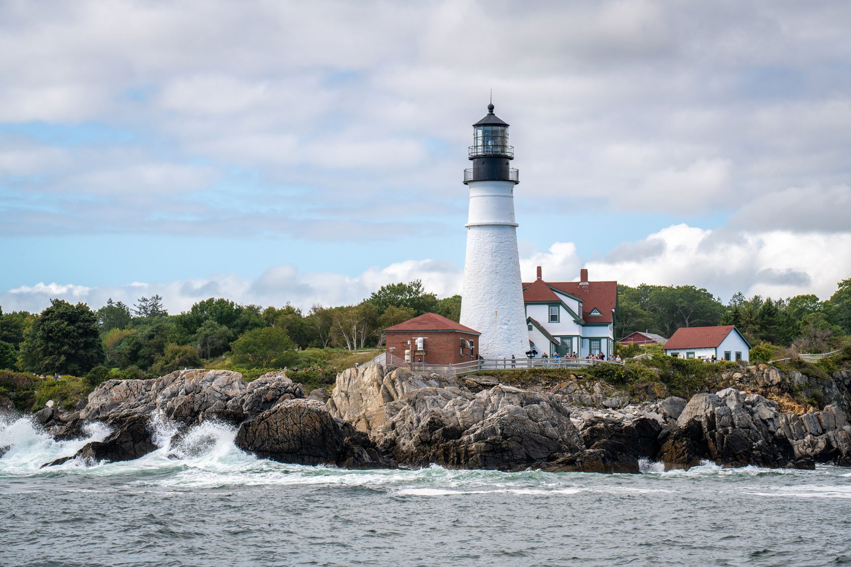A lighthouse sits near a rocky shoreline.
