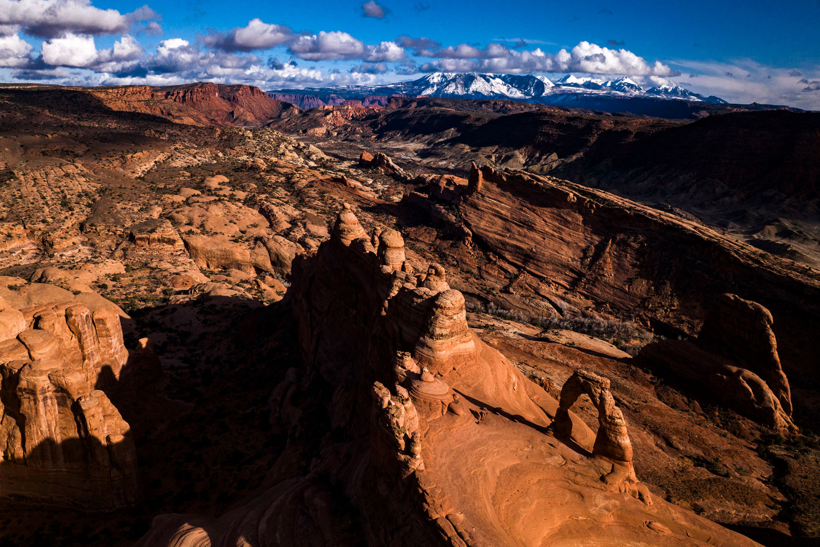 Delicate Arch gives way to a vast expanse of red rocks and snow-capped mountains in the distance at Arches National Park in Utah.