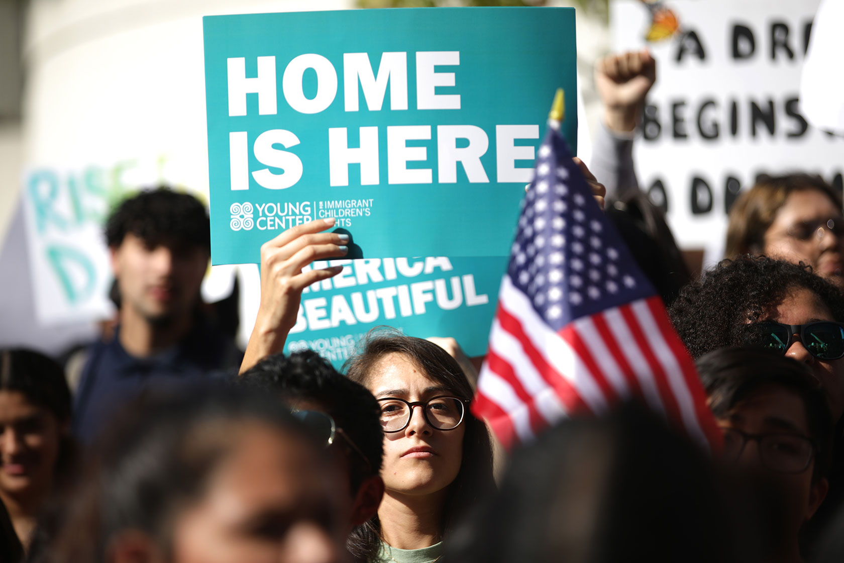 Person holding up sign that reads Home Is Here