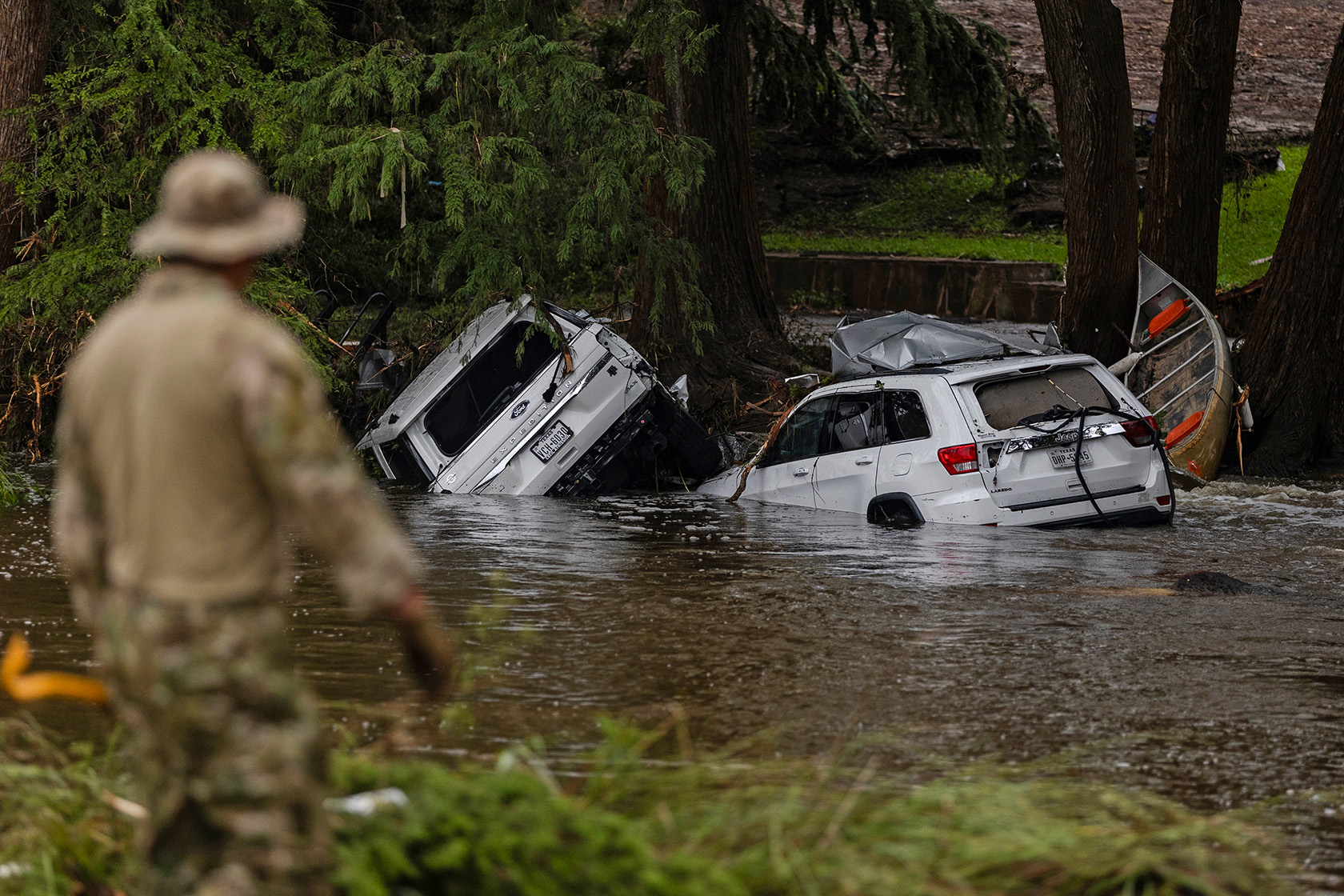 Vehicles sit submerged as a search and rescue worker looks through debris for any survivors.