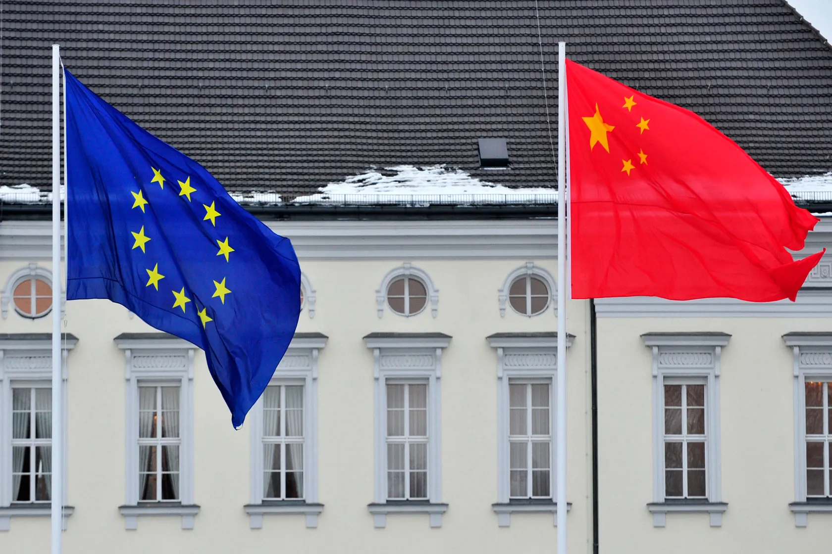 The European Union flag, with a blue field and 10 stars that form a circle, flies next to the Chinese flag, which has a red field and four smaller stars making a semicircle around a fifth, larger star.