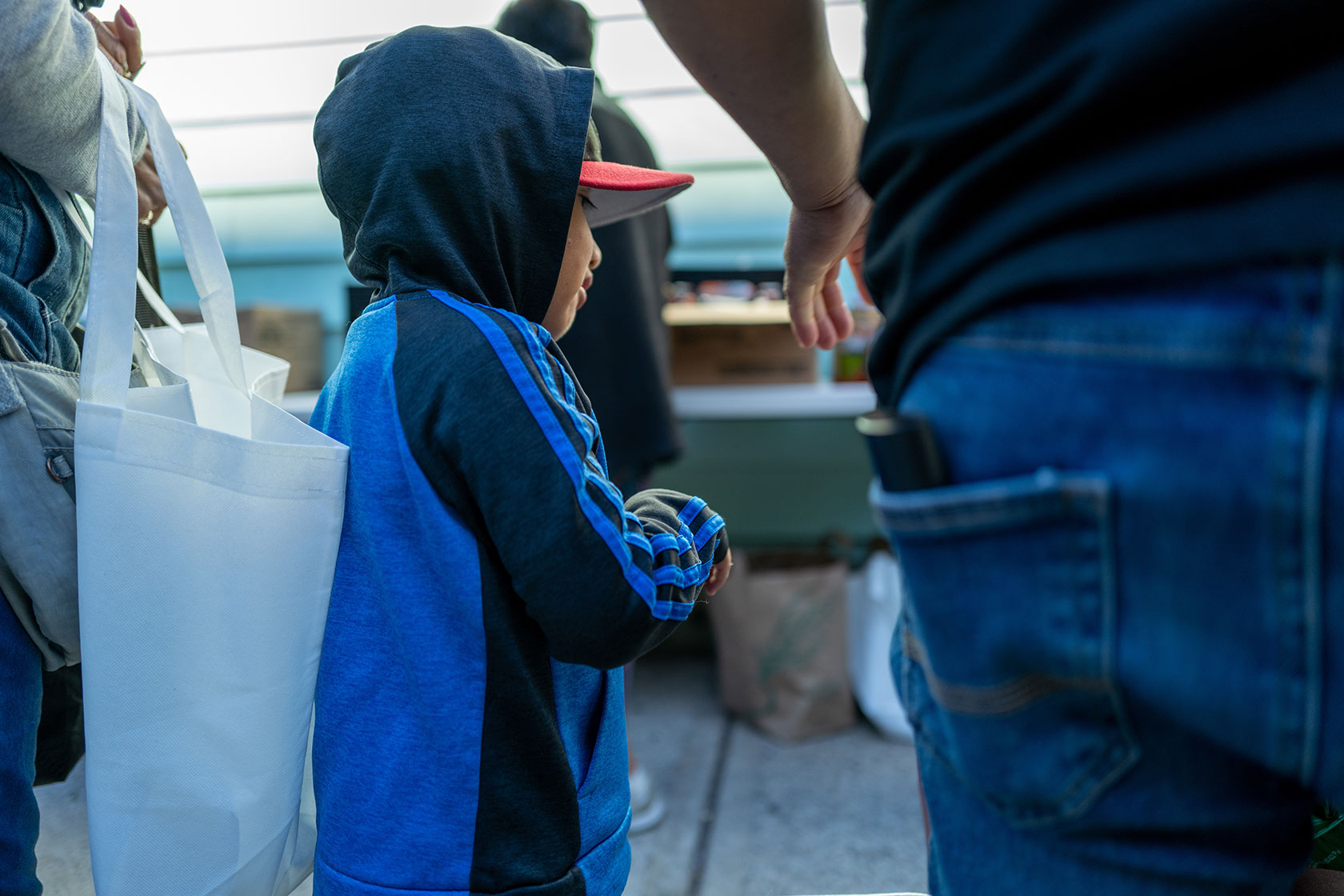 Profile of young boy, wearing hoodie and cap, standing in line