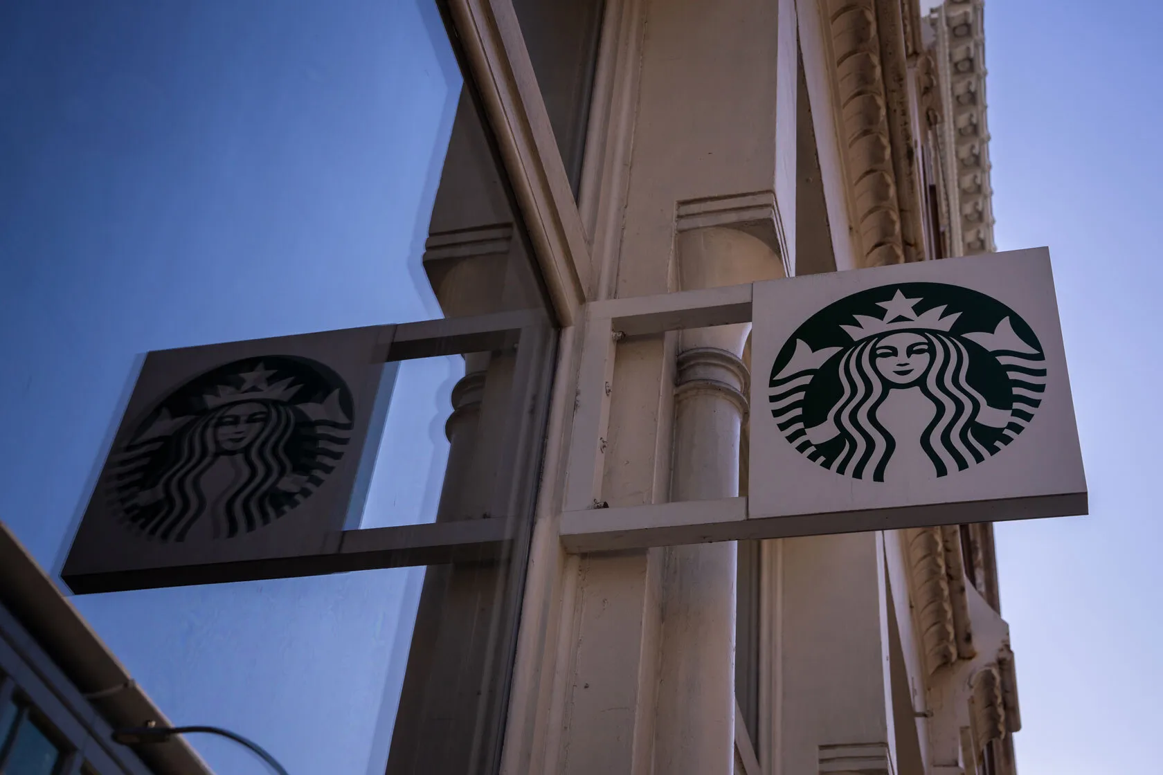 A Starbucks sign is reflected in the window as Starbucks employees, union members and supporters strike outside of a Starbucks store.