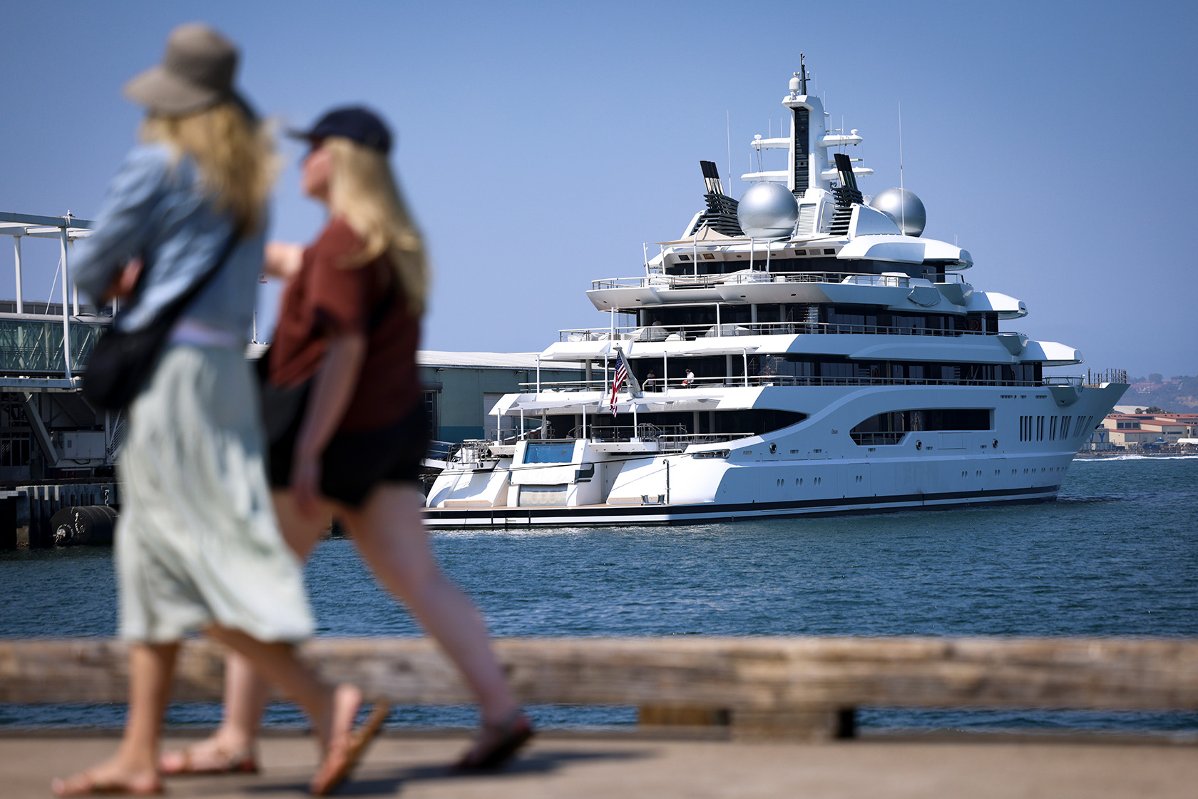 A pair walks past a large superyacht.