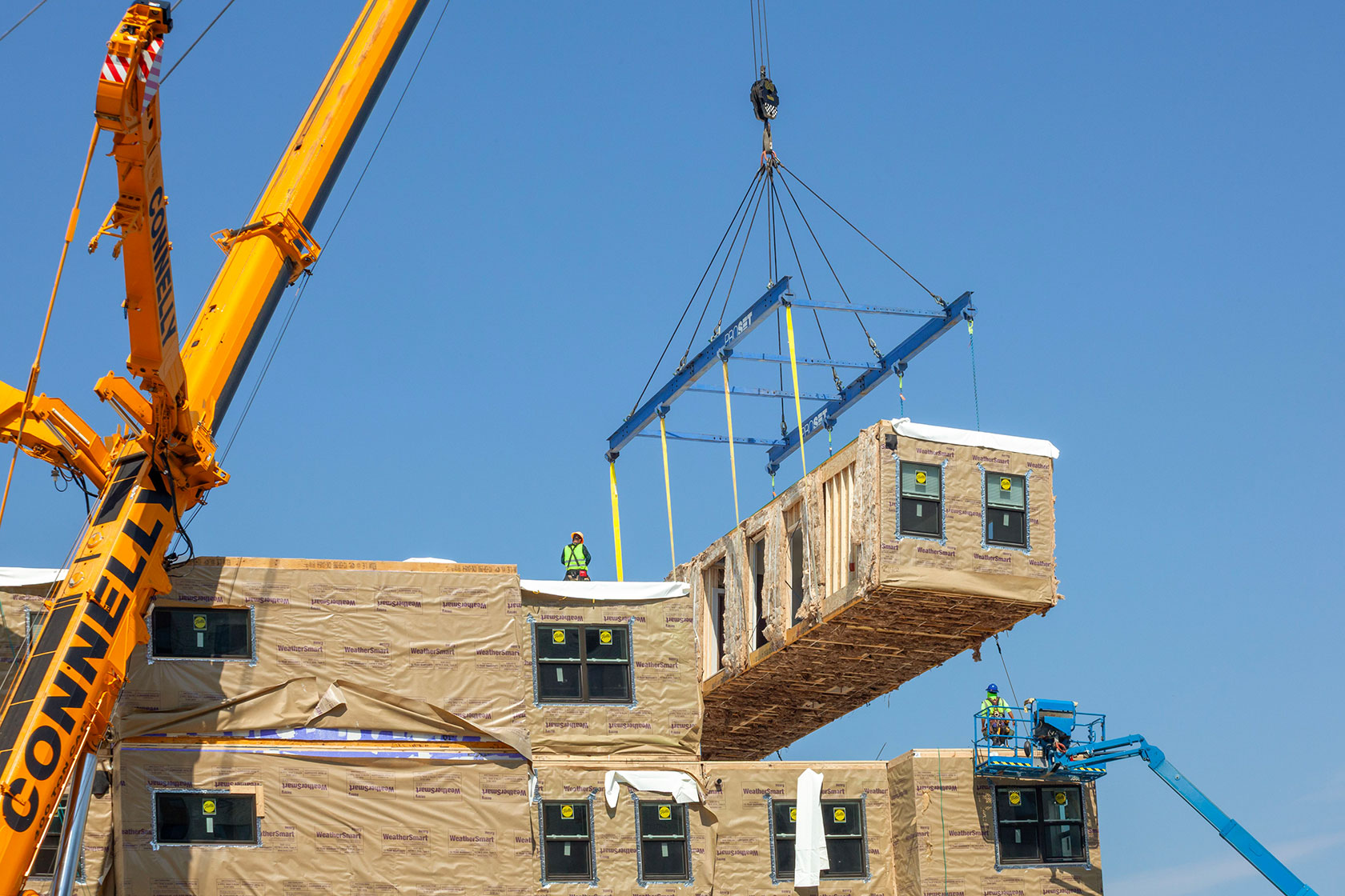 Crane lowering portion of building with worker on roof