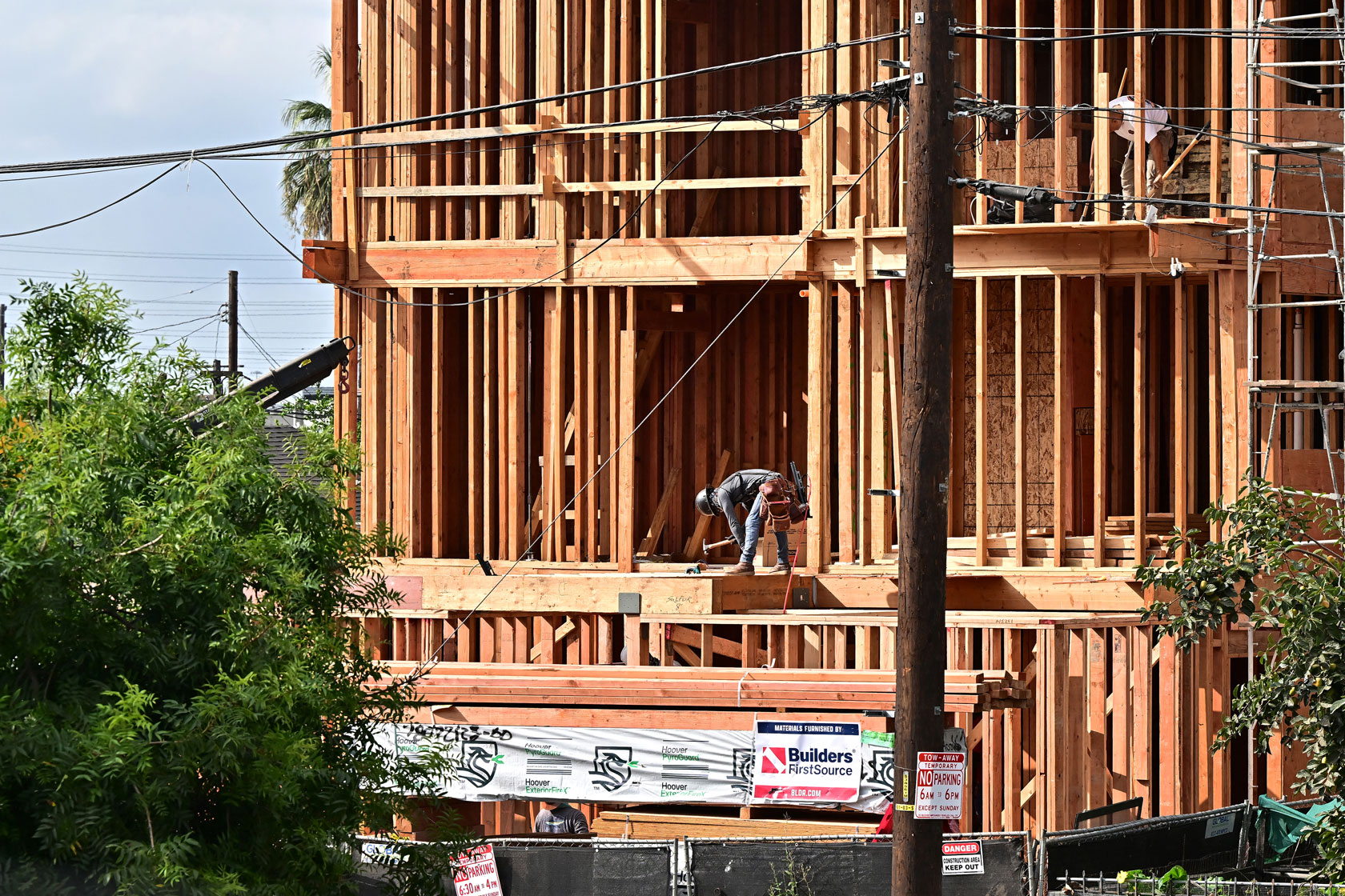Two construction workers, each on a different floor, work on the frame of a building.