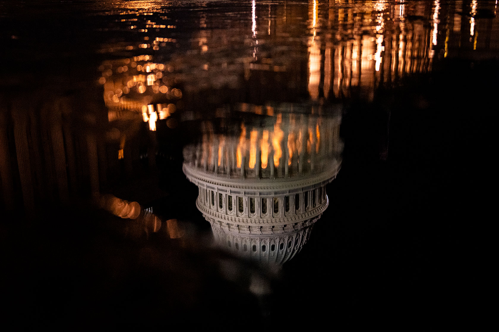 Capitol building reflected upside in water against a dark sky