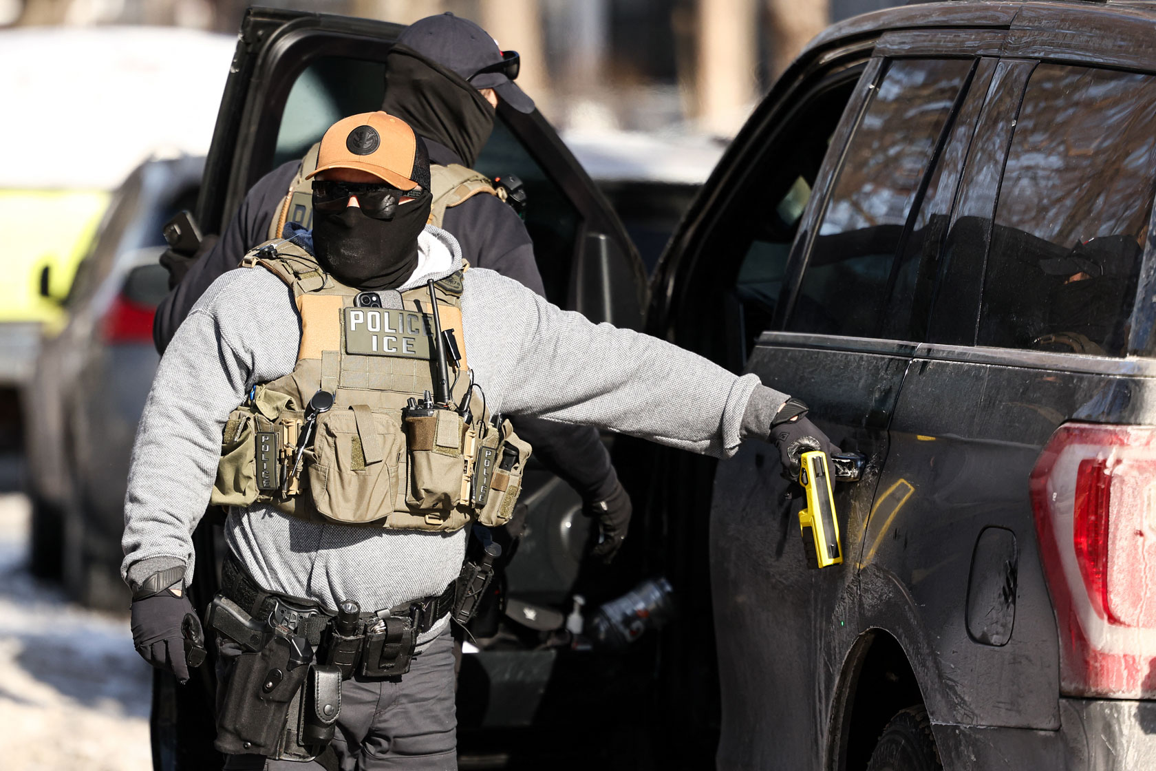 Masked federal agents outside a vehicle.